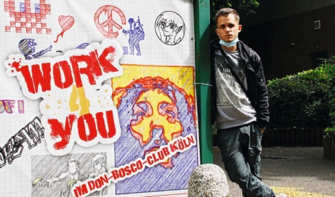 Junger Mann steht vor Wand mit bunten Aufschriften des Projekts Work4 You. 